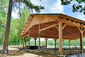 Ein hölzernes Pavillon mit geneigtem Dach, auf Kies gegründet und von Bäumen umgeben.