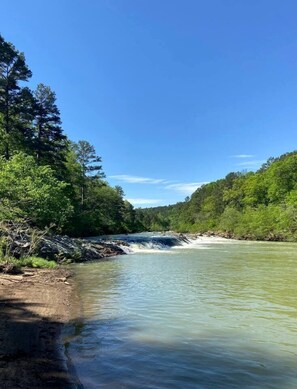 Une rivière avec une cascade, entourée d’une forêt dense et sous un ciel bleu clair.
