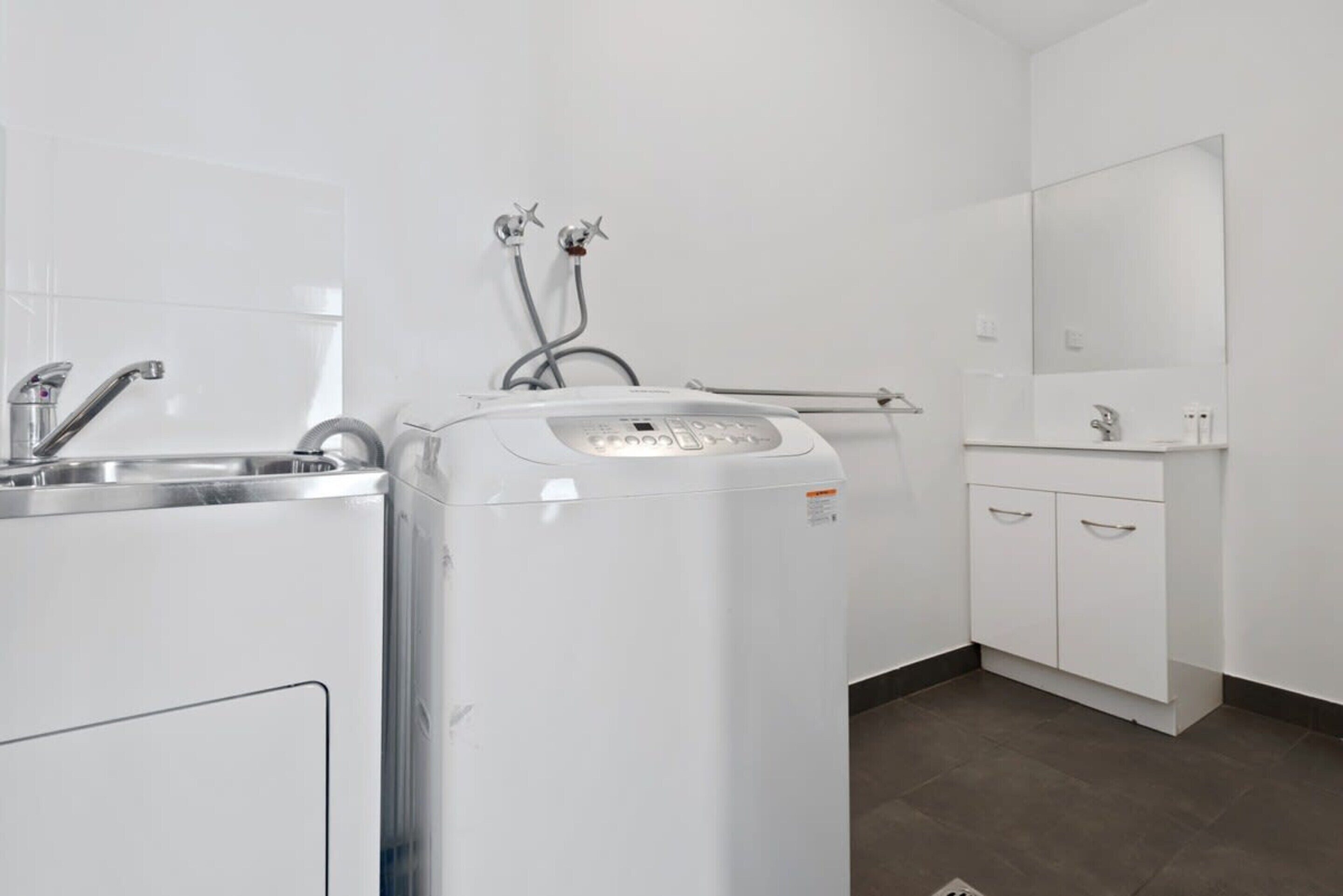 Une salle de bain moderne équipée d’un lave-linge intégré, d’un lavabo et d’un miroir.