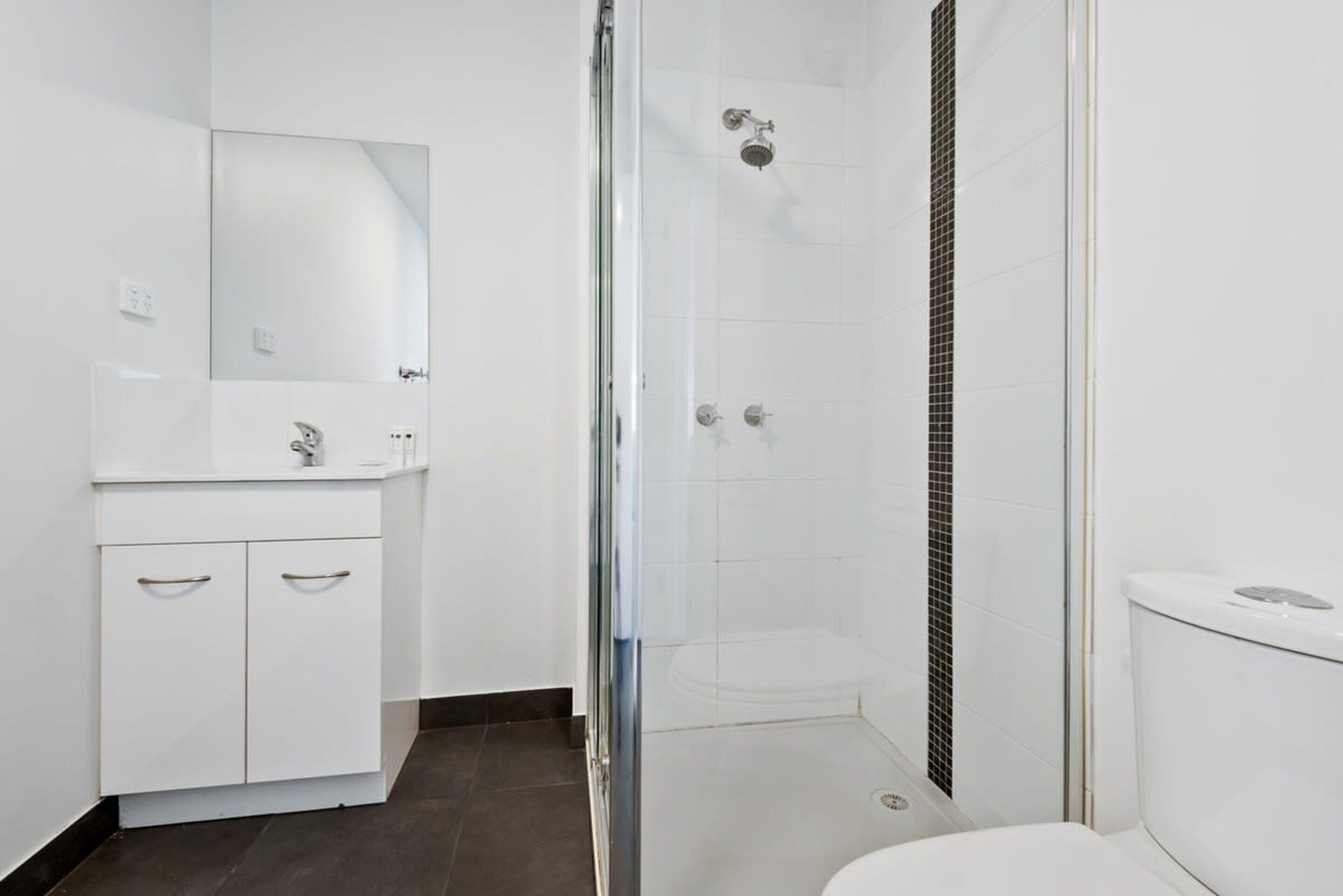 A modern bathroom with a glass shower enclosure, a white sink with a mirror, and a toilet.
