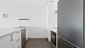 A modern kitchen with white cabinetry, a stainless steel refrigerator, a dishwasher, and a tiled backsplash. - Executive and Spacious Apartment With Balcony (Melbourne)