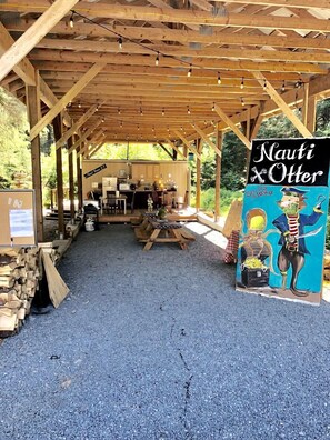 A covered outdoor area with a wooden structure, a sign reading 'Nauti & Otter,' and a gravel floor.