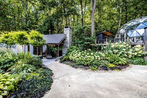 A modern house with a stone chimney, a covered patio, and a garden with various plants. - Magical Family Cabin with Breathtaking Beauty and Modern Interior in Alabama (Scottsboro)