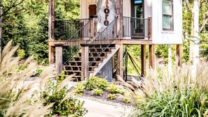 Ein Baumhaus mit Holzfassade, einem Balkon und einer Treppe, die hinaufführt.