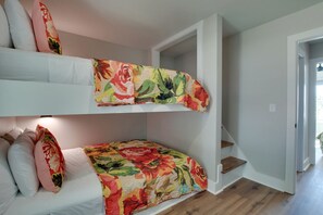 A bunk bed room with a floral quilt, white walls, and a staircase.
