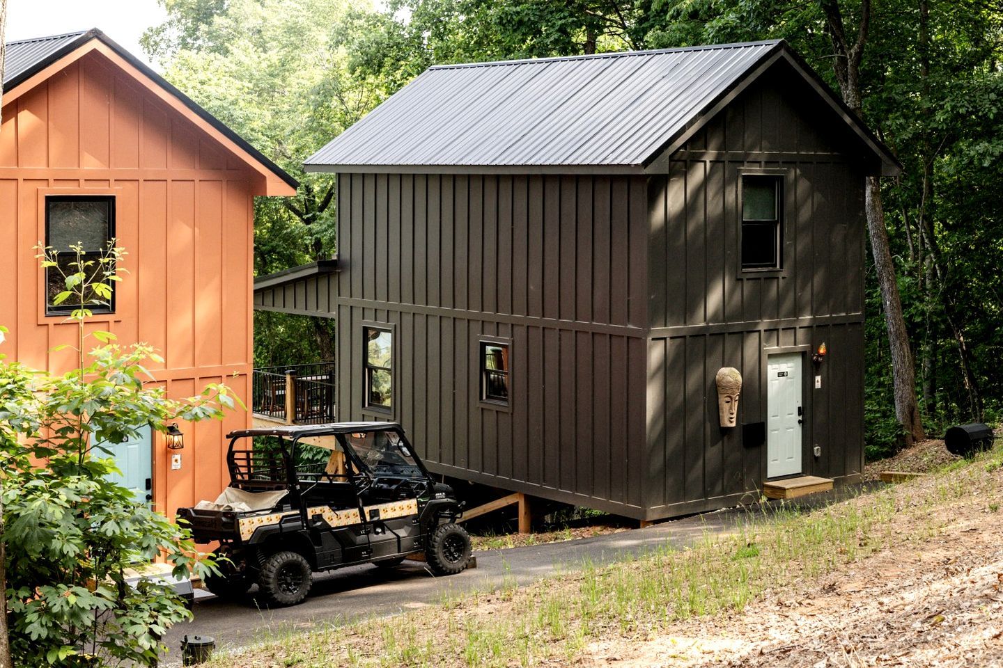 Een chalet met twee verdiepingen, een metalen dak, een voertuig ervoor en een klein terras.