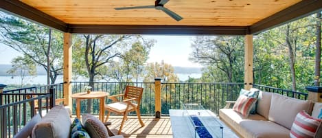 Un espacio al aire libre cubierto con mesa, sillas y sofá, con vistas a un cuerpo de agua y árboles.