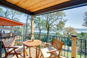 Terraza de madera con mesa y sillas, con vistas a un paisaje con árboles y un cuerpo de agua.