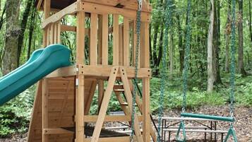 A wooden play structure with a slide and swings in a wooded area.