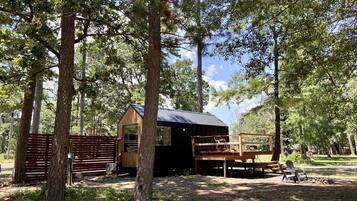 A rustic cabin with a wooden deck and a small porch, surrounded by trees.