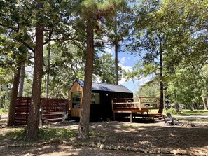 Un chalet rustique doté d’une terrasse en bois et d’un petit porche, entouré d’arbres.