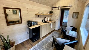 Cocina compacta con armarios de madera, un lavamanos y una pequeña zona de comedor con una silla y una mesa.