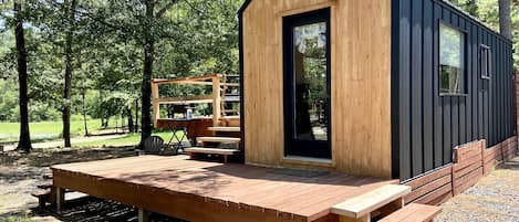 Una cabaña de madera pequeña con terraza, un banco y una mesa.