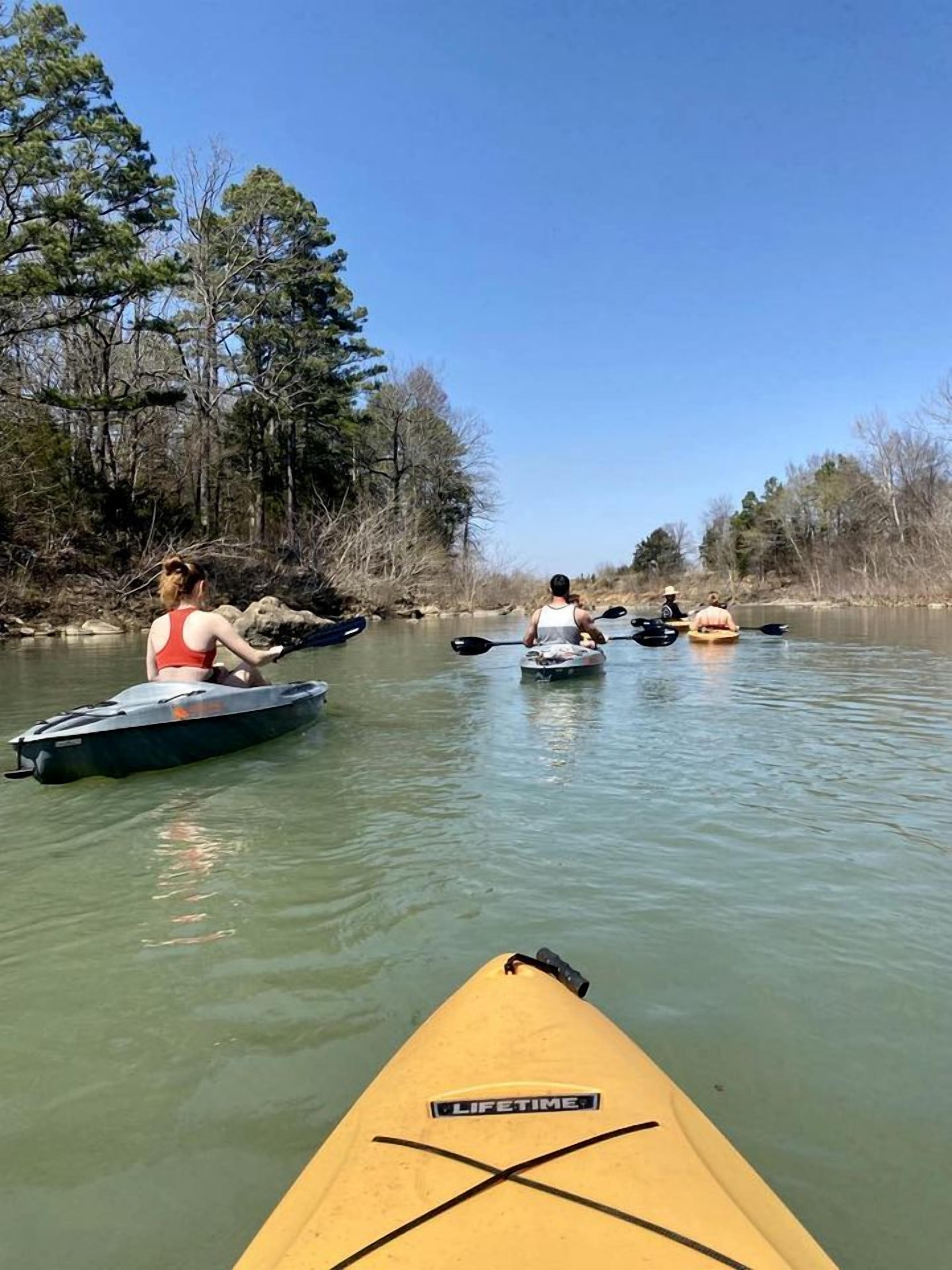 A river scene with kayaks and canoes, surrounded by trees.