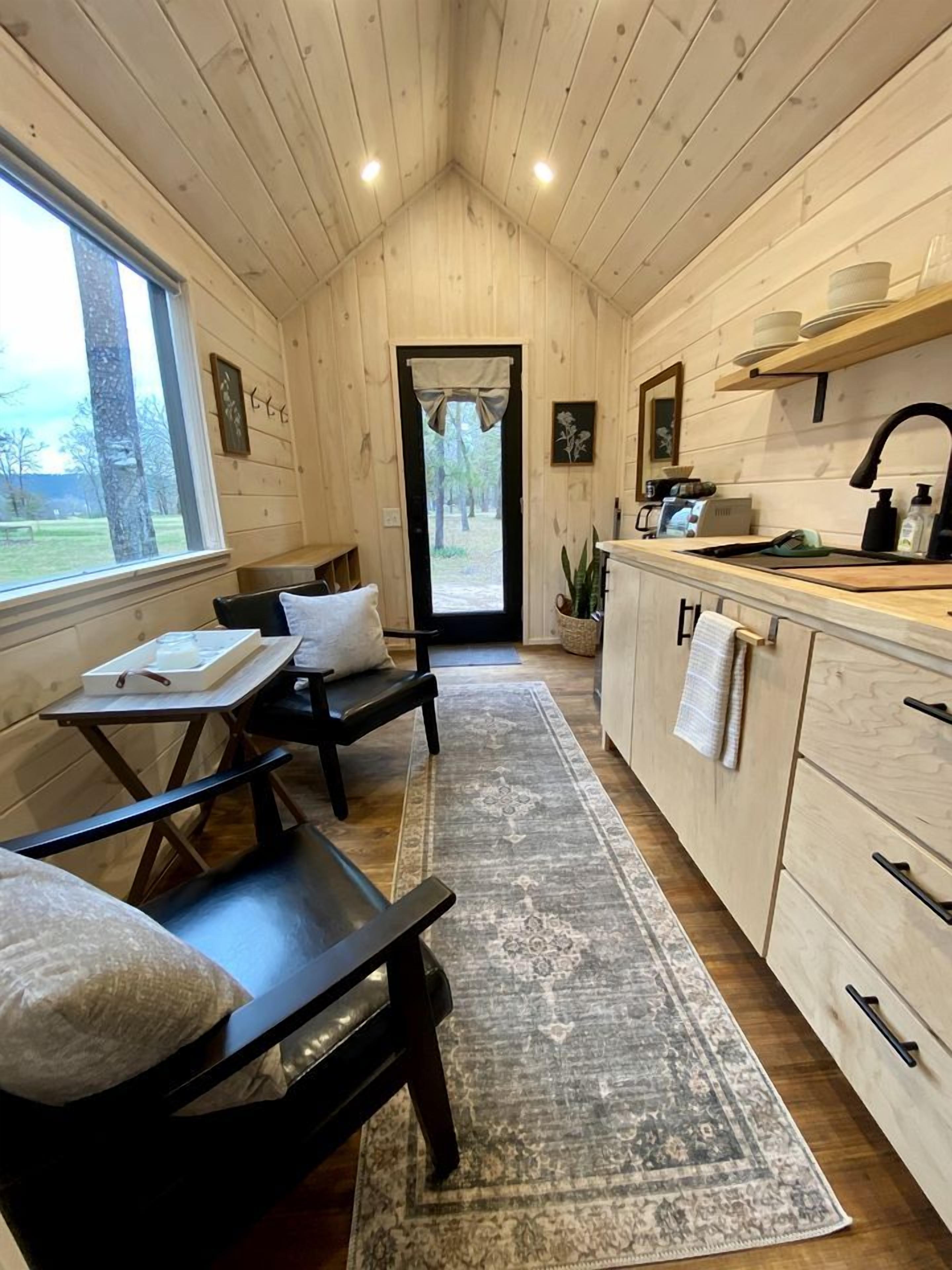 A cozy cabin interior with a dining area, a kitchen with a sink and cabinets, and a view through a door.