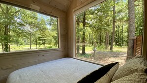 Un dormitorio con una cama grande, paredes de madera y vistas a un bosque a través de amplios ventanales.