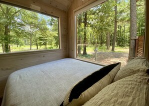 Une chambre à coucher avec un grand lit, des murs en bois et une vue sur une forêt, visible à travers de grandes fenêtres.