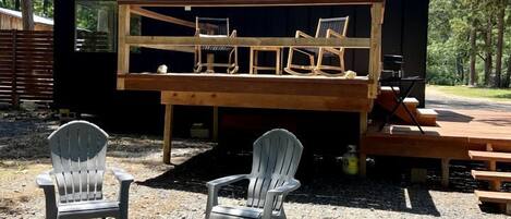 A cabin with a deck, two Adirondack chairs, and a fire pit.