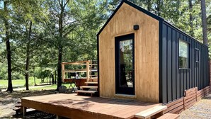 Una cabaña de madera pequeña con terraza, un banco y una mesa.