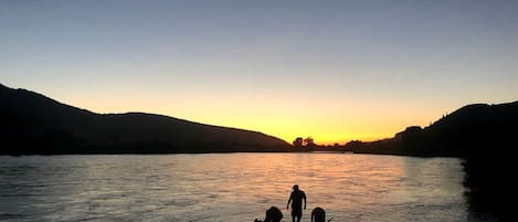Une rivière au coucher du soleil, avec des personnes et un bateau sur la rive.