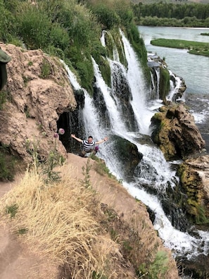 Una cascada con una persona de pie sobre una formación rocosa.