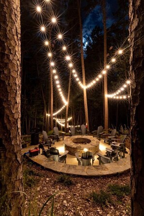 A circular outdoor seating area with stone flooring, surrounded by trees and string lights.