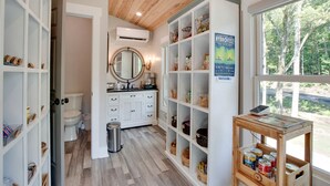 A bathroom with a toilet, sink, vanity, and shelves with various items. - Off-grid Tree House Suitable for Four in Alabama (Scottsboro)