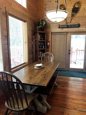 Un interior de madera con una mesa de comedor, sillas, una araña, un letrero de bienvenida y una puerta que da al exterior.