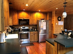 Cocina con gabinetes de madera, electrodomésticos de acero inoxidable y encimera negra.