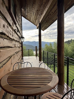 A wooden deck with a table and chairs, overlooking a mountainous landscape.