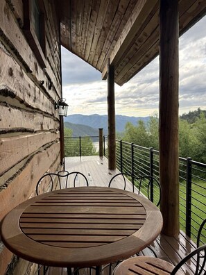 Terraza de madera con una mesa y sillas, con vista a un paisaje montañoso.