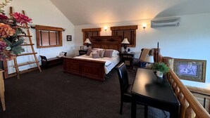 Une chambre à coucher avec un lit, des tables de chevet, un bureau et une chaise. On y trouve également une échelle, une plante en pot et un cadre photo accroché au mur.
