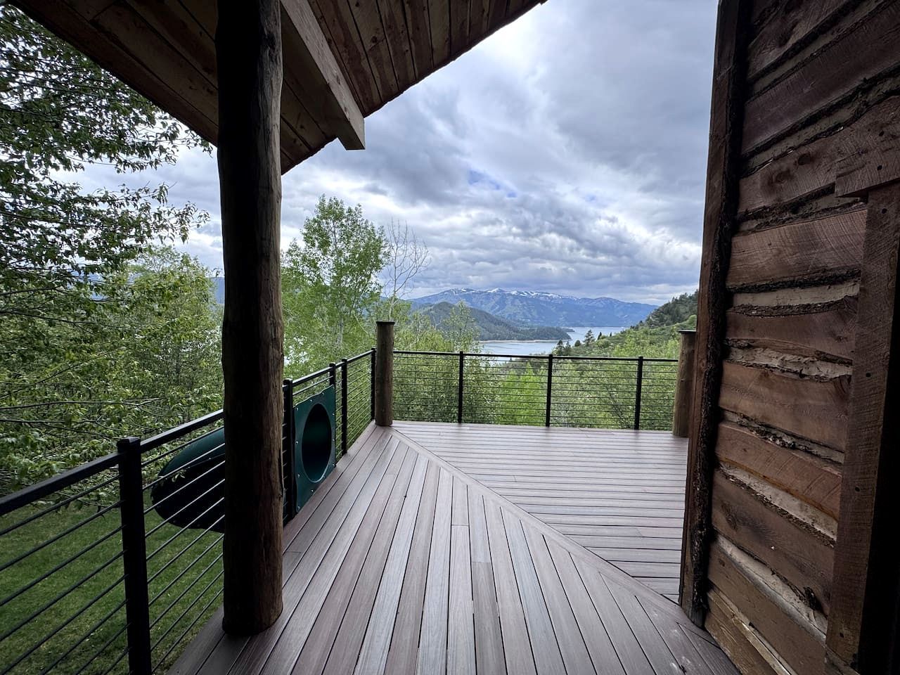A wooden deck with a metal railing, overlooking a lake and mountains.