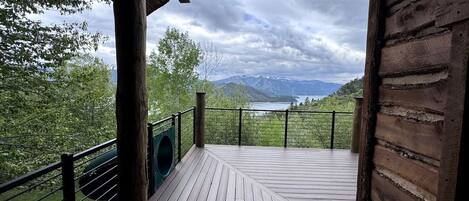 A wooden deck with a metal railing, overlooking a lake and mountains.