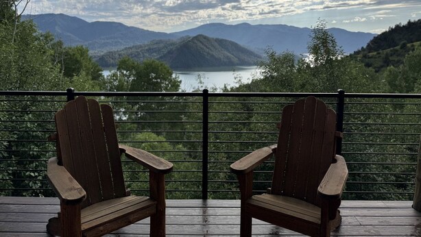 Deux fauteuils Adirondack en bois, placés sur une terrasse en bois, offrent une vue sur les montagnes et un lac.