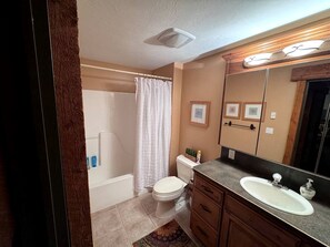 A bathroom with a toilet, sink, vanity, shower curtain, and a mirror.