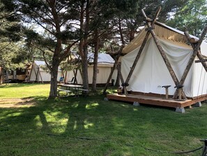 A campsite with tents, a picnic table, and a wooden deck. - Luxury Safari Tent with Private Bathroom in Swan Valley, Idaho near Palisades Lake (Irwin)