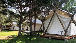 A campsite with tents, a picnic table, and a wooden deck. - Luxury Safari Tent with Private Bathroom in Swan Valley, Idaho near Palisades Lake (Irwin)