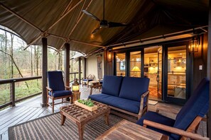 Una terraza techada al aire libre con asientos, una mesa y vista al interior.