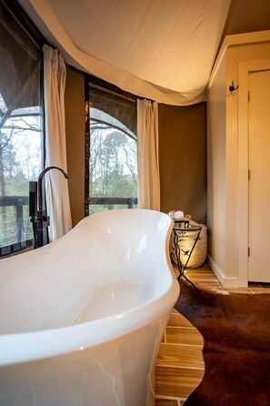 Ein modernes Badezimmer mit einer freistehenden Badewanne, einer Holzbank, einem großen Fenster mit Vorhängen und einer Tür.