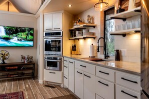 A modern kitchen with white cabinetry, stainless steel appliances, and a flat-screen TV.
