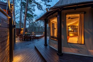 Una terraza de madera con un jacuzzi, un comedor y un dormitorio con ventana que da a la terraza.