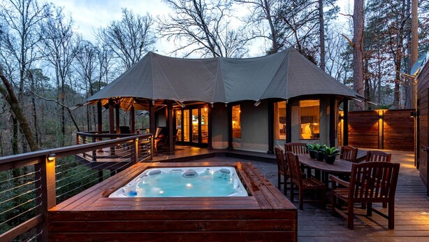 Un bain à remous sur une terrasse en bois, avec un espace salon couvert et une vue sur la forêt.