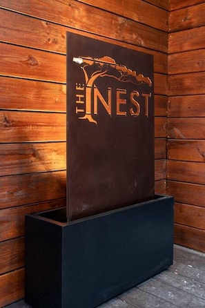 Eine Holzwand mit einem Schild, auf dem in Goldbuchstaben 'THE NEST' steht.