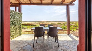 Une terrasse extérieure avec une table et des chaises, une pergola en bois et une vue sur la campagne.
