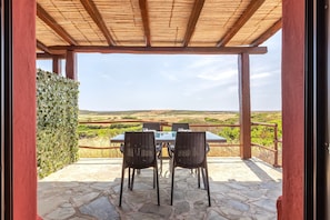Un patio al aire libre con mesa y sillas, una pérgola de madera y vistas al campo.