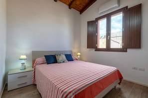 A bedroom with a bed, nightstands, a window with shutters, and an air conditioning unit.