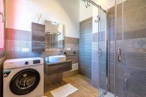 A modern bathroom with a washing machine, a sink, a mirror, and a shower area.