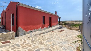 A red building with a stone-paved entrance and a clear sky. - 'Villetta Wild' Apartment with Sea View, Shared Terrace and Air Conditioning (Stintino)