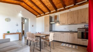 A modern kitchen with wooden cabinets, a dining table with chairs, and a red curtain. - 'Villetta Wild' Apartment with Sea View, Shared Terrace and Air Conditioning (Stintino)